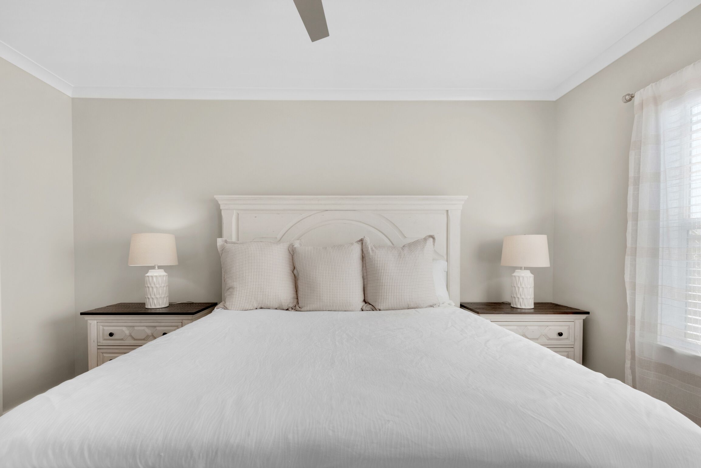 A bedroom with a large bed, two bedside tables with lamps, and a ceiling fan.