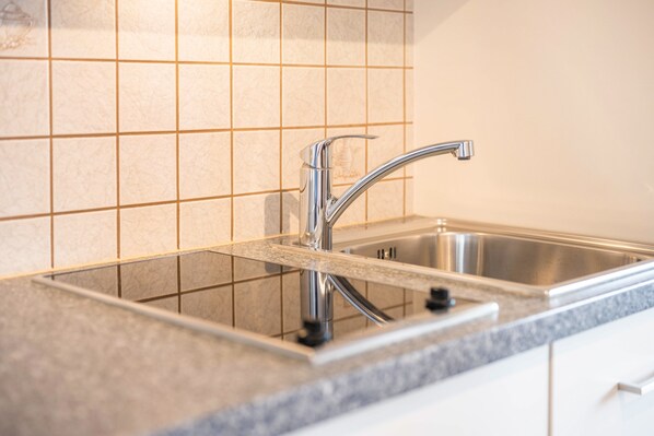 A kitchen with a stainless steel sink, a faucet, and a tiled backsplash.