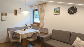 A cozy room with a dining table, chairs, a sofa, a clock, and a window with curtains. - Charming Apartment “Haselstaude - Abendrot” with Mountain View, Wi-Fi, Terrace & Garden; Parking Available (Meransen/Mühlbach)