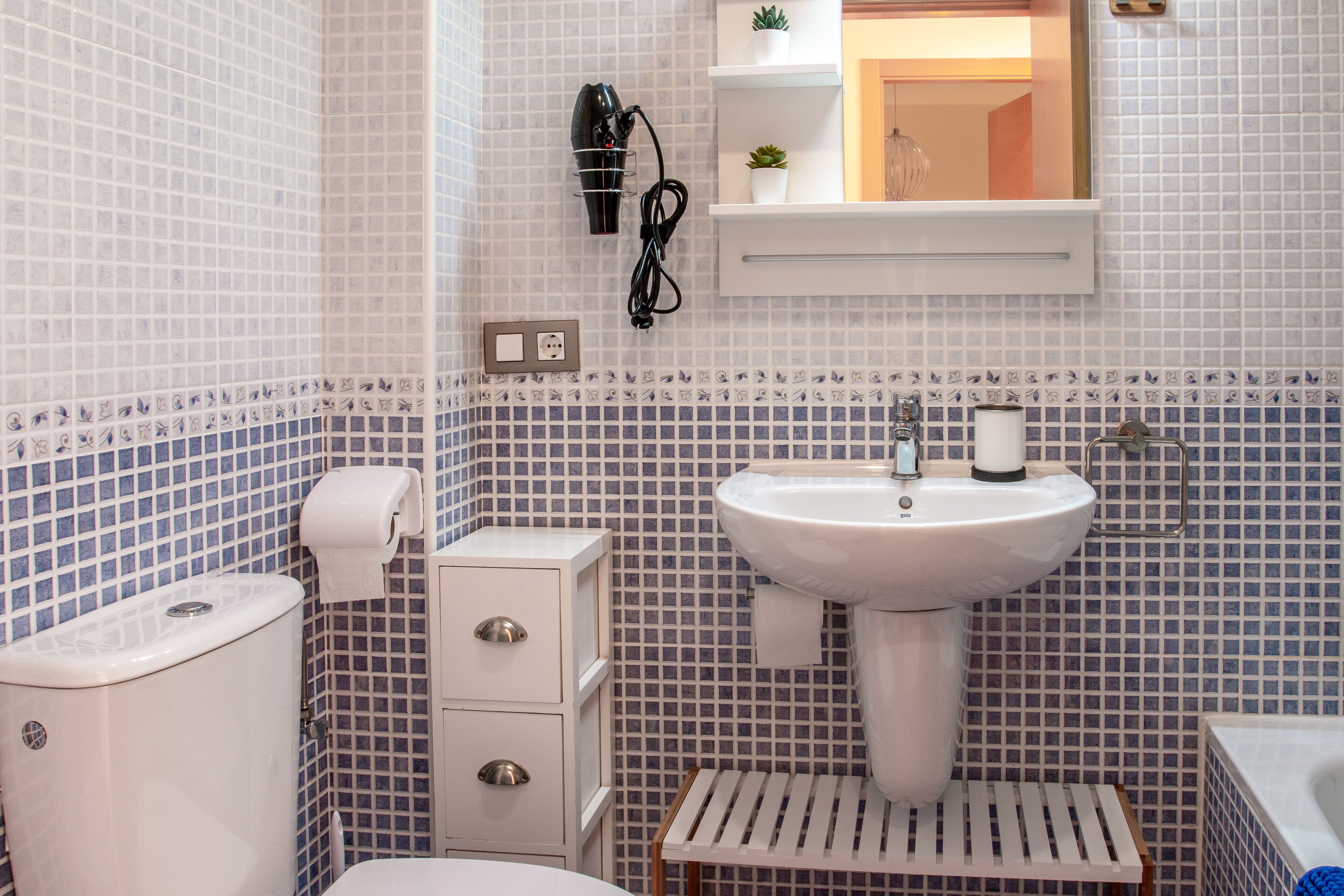A bathroom with a white sink, toilet, and bidet, tiled in blue and white patterns.