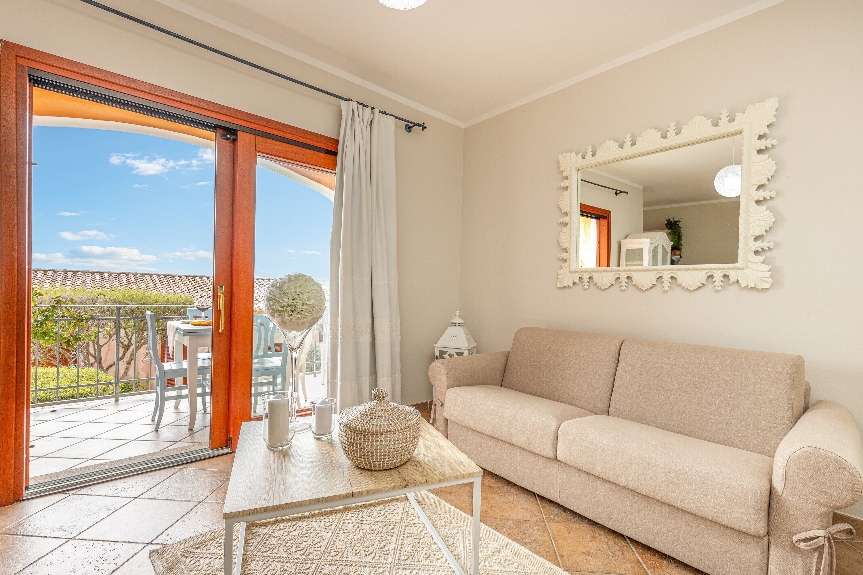 Ein Wohnzimmer mit einer Couch, einem Tisch mit Dekoration, einem Spiegel und Blick ins Freie.