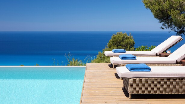 Terraza de madera con tres sillas reclinables y una piscina.