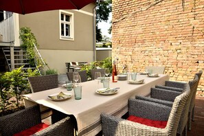 A dining area with a long table set for four, surrounded by wicker chairs with red cushions. - Landidyll Schwielowsee "Villa Siebenhaar" - Coziness at the Schwielowsee (Schwielowsee)
