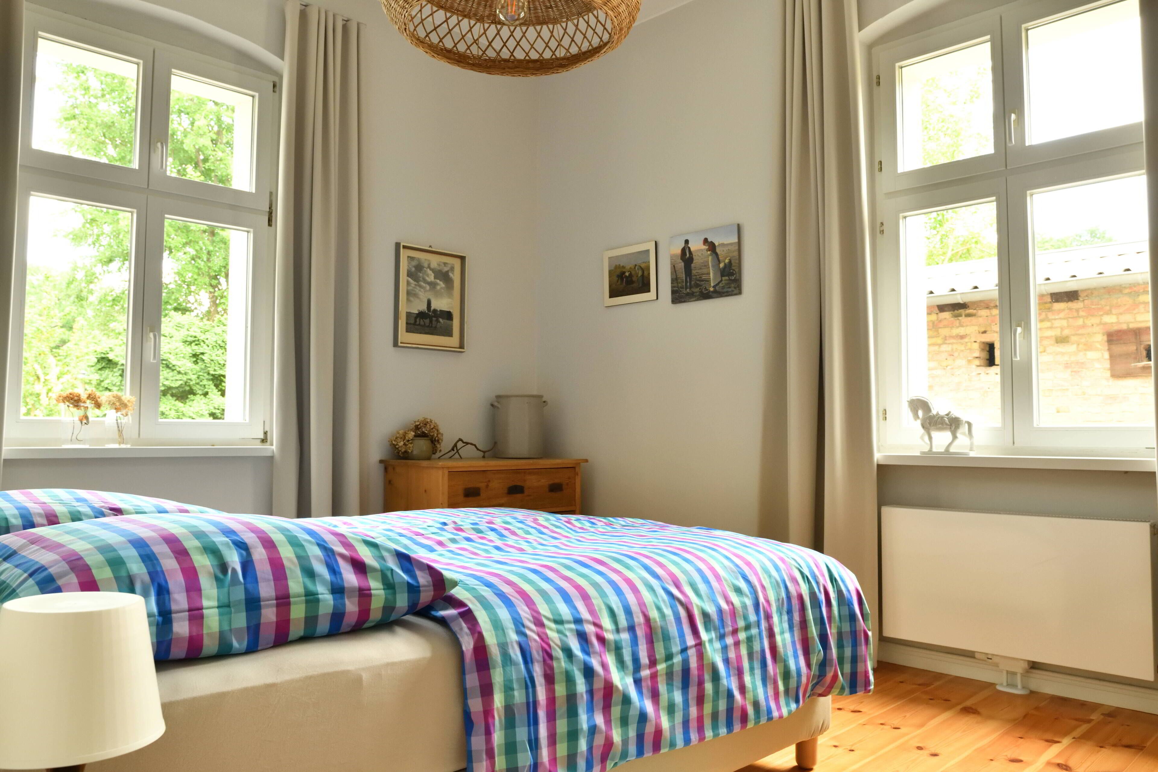 A bedroom with a bed, a nightstand, a lamp, and two windows with curtains.