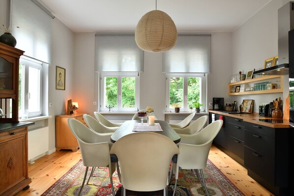A modern kitchen with a dining area, featuring a wooden table, white chairs, and a hanging light fixture. - Landidyll Schwielowsee "Villa Siebenhaar" - Coziness at the Schwielowsee (Schwielowsee)