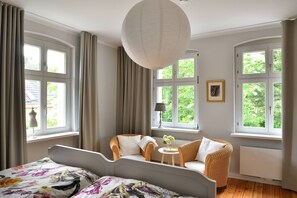 A bedroom with a bed, two chairs, a table with flowers, and large windows. - Landidyll Schwielowsee "Villa Siebenhaar" - Coziness at the Schwielowsee (Schwielowsee)