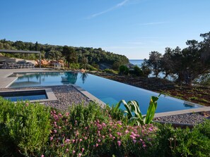 Ein Pool mit Blick auf das Meer, umgeben von Grünflächen und einer kleinen Sitzecke.