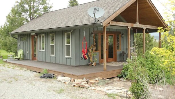 Une cabane rustique dotée d’une véranda, d’une antenne parabolique et d’un petit jardin.