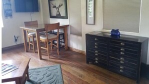 Une pièce comprenant une table et des chaises en bois, une commode noire avec des tiroirs et deux tableaux encadrés accrochés au mur.