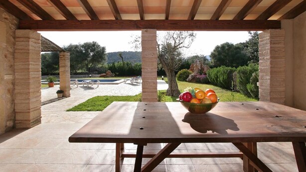 Ein Holztisch mit Obstschale unter einer Pergola mit Blick auf Pool und Garten.