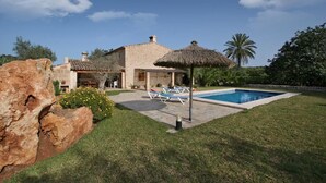 Eine Steinvilla mit Swimmingpool, Sitzgelegenheiten im Freien und einer großen Felsformation.
