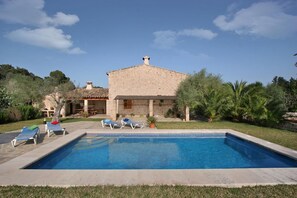 A stone building with a swimming pool, lounge chairs, and a garden.