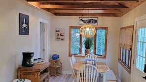 A cozy dining area with a wooden table and chairs, a coffee machine, and a wicker basket. - Renovated Ridgewood Bay House (Lower Township)