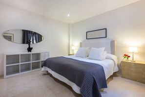 A bedroom with a bed, a bedside table with a lamp, a nightstand with a lamp, a large mirror, and a wall-mounted picture.