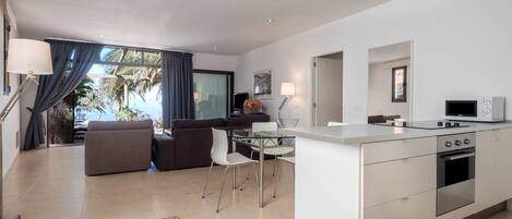Una cocina moderna con una isla central, un comedor con mesa de vidrio y una sala de estar con sofá y sillones.