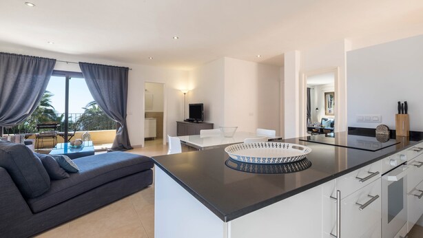 A modern kitchen with a central island, a dining area with a white table and chairs, and a sofa with a view to the outdoors. - Apartment “La Casita” with Sea View, Pool, Wi-Fi, Terrace & Balcony (Adeje)