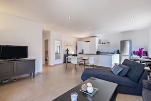 A modern living room with a flat-screen TV, a sofa, a coffee table with decorative items, and a kitchen area in the background. - Apartment “La Casita” with Sea View, Pool, Wi-Fi, Terrace & Balcony (Adeje)