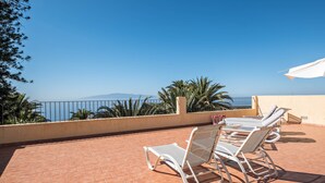 A terrace with white sun loungers and a table, overlooking a coastal view with palm trees and mountains. - Apartment “La Casita” with Sea View, Pool, Wi-Fi, Terrace & Balcony (Adeje)