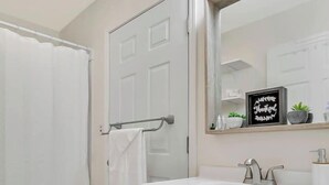 Un baño con ducha, inodoro, tocador y espejo con un letrero.