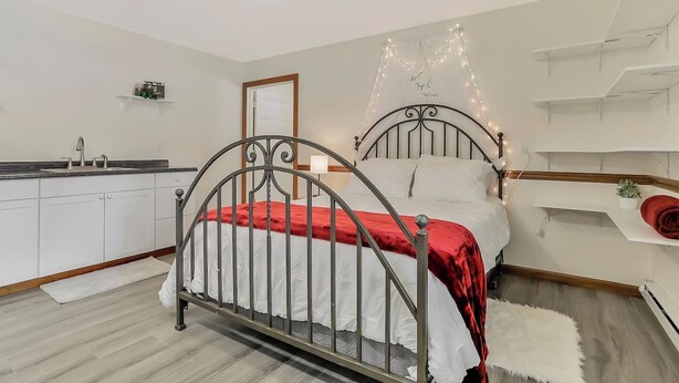 Un dormitorio con una cama, ventilador de techo, mesita de noche, pequeña planta y estante en la pared.