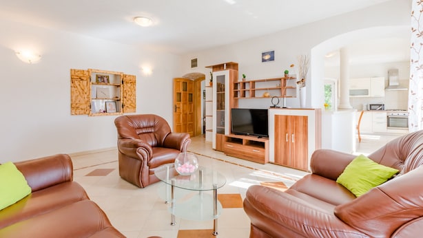 A modern living room with leather sofas, a glass coffee table, wooden cabinets, and a TV.