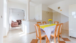 A dining area with a table set for four, surrounded by wooden chairs, a white tablecloth, and a vase with yellow flowers.