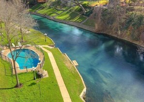 Una piscina con una fuente de agua cristalina azul, rodeada por un césped cuidado y un sendero para caminar.