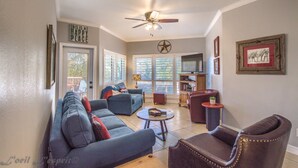 A living room with a blue sofa, a brown leather chair, a round coffee table, and a ceiling fan. - Cowboy Corral Ic 112 2 Bedroom Condo by RedAwning (New Braunfels)