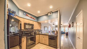 A kitchen with a black refrigerator, stove, microwave, and dishwasher. There is a blue wall with a sign that reads "Don'ts with Texas." - Cowboy Corral Ic 112 2 Bedroom Condo by RedAwning (New Braunfels)