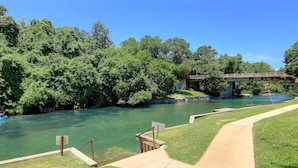 A river with a wooden bridge, a concrete walkway, and lush greenery. - Cowboy Corral Ic 112 2 Bedroom Condo by RedAwning (New Braunfels)