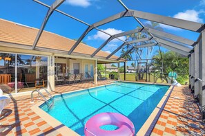 Zona de piscina con cerramiento de vidrio, suelo de baldosas y un flotador hinchable rosa.