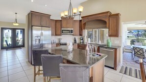 A modern kitchen with a central island, stainless steel appliances, and a dining area with a view. - Southern Exposure Waterfront Home | Pool & Dock (Marco Island)