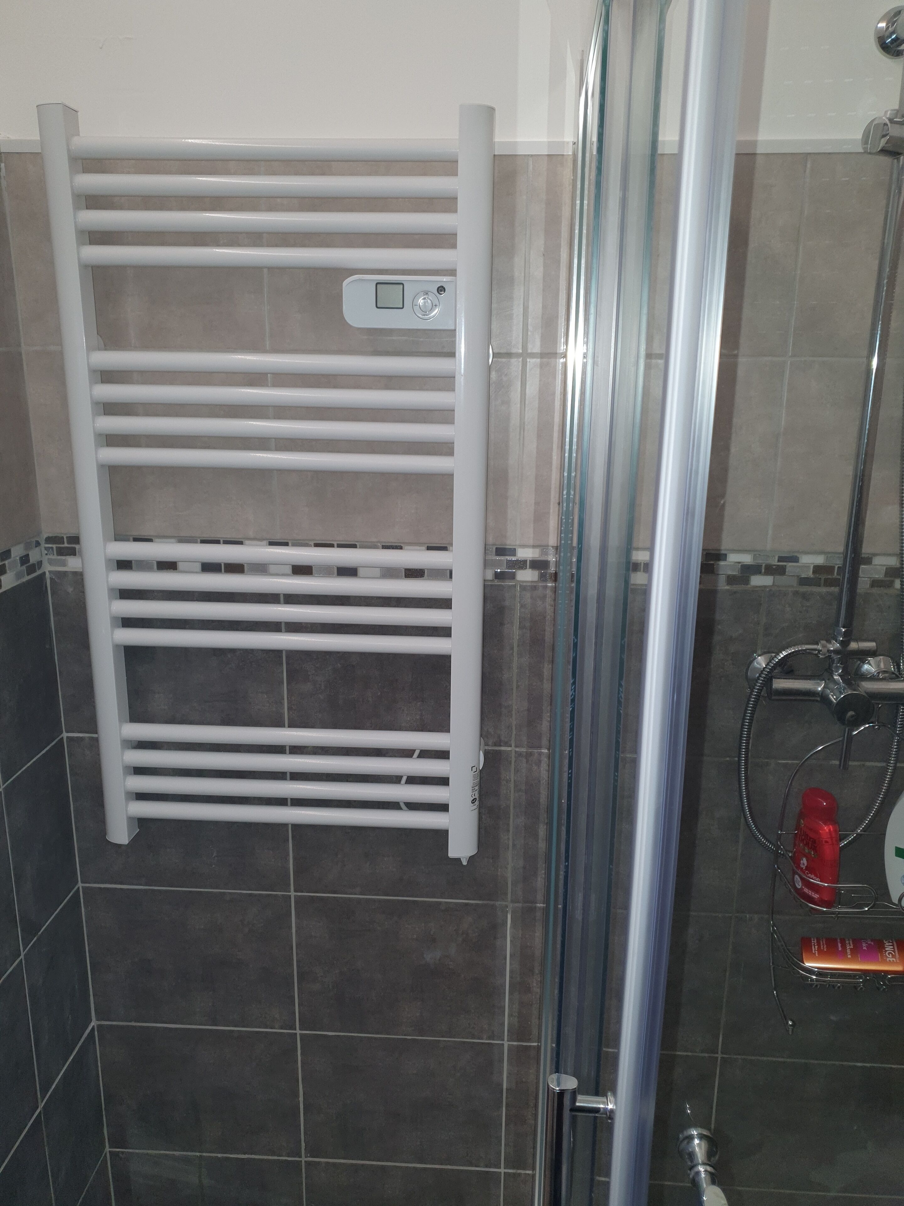 Une salle de bain avec un porte-serviettes blanc, une cabine de douche en verre et un pommeau de douche.