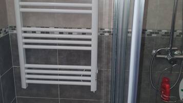 Une salle de bain avec un porte-serviettes blanc, une cabine de douche en verre et un pommeau de douche.