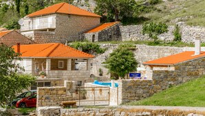 A stone building with a red-tiled roof, a swimming pool, and a sign indicating a hotel. - Stone House Kuna (Konavle)