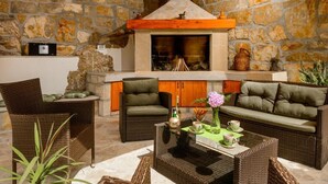 An outdoor seating area with wicker furniture, a stone wall, and a fireplace. - Stone House Kuna (Konavle)