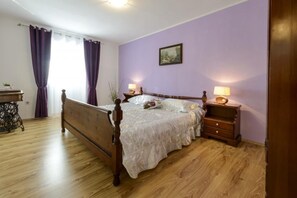 A bedroom with a wooden bed, two bedside tables with lamps, a small table with a lamp, and a painting on the wall. - Stone House Kuna (Konavle)