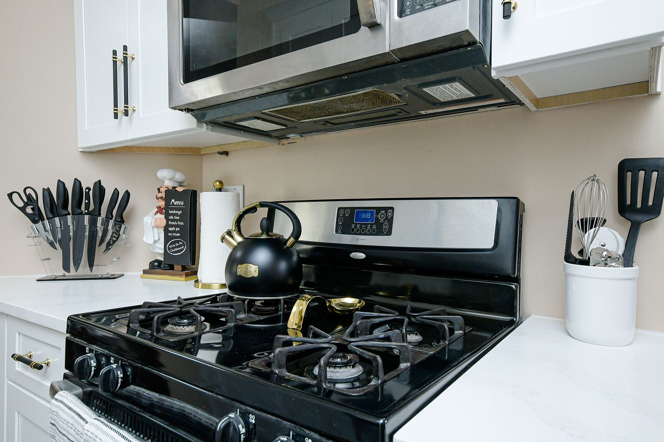 A kitchen with a black stove, stainless steel microwave, and white cabinets.