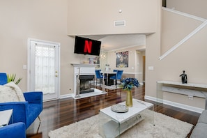 A modern living room with a fireplace, a mounted TV, and a dining area with blue chairs. - Summerhill Sensation (townhouse downtown Atlanta) (Atlanta)