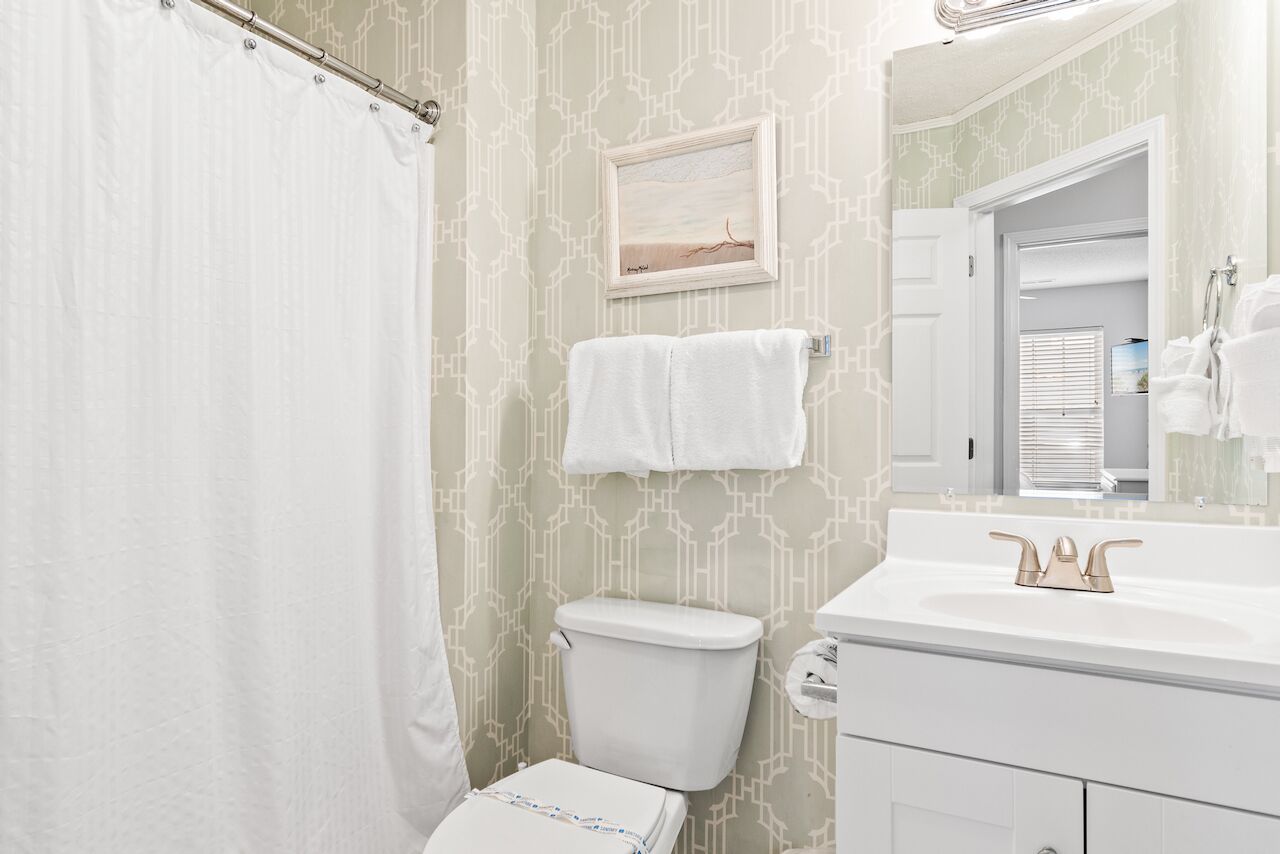 Une salle de bain avec des toilettes, un lavabo doté d’un robinet doré, un rideau de douche et un tableau encadré accroché au mur.
