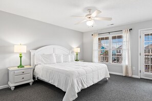 A bedroom with a bed, two bedside tables with lamps, a ceiling fan, and a window with blinds.