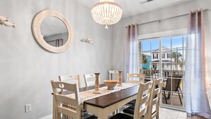 A dining area with a wooden table and chairs, a chandelier, a round mirror, and a view of the outside through large windows. - Walk to Surfside Beach from This 4-Bedroom Condo w/ Resort Pool (Surfside Beach)