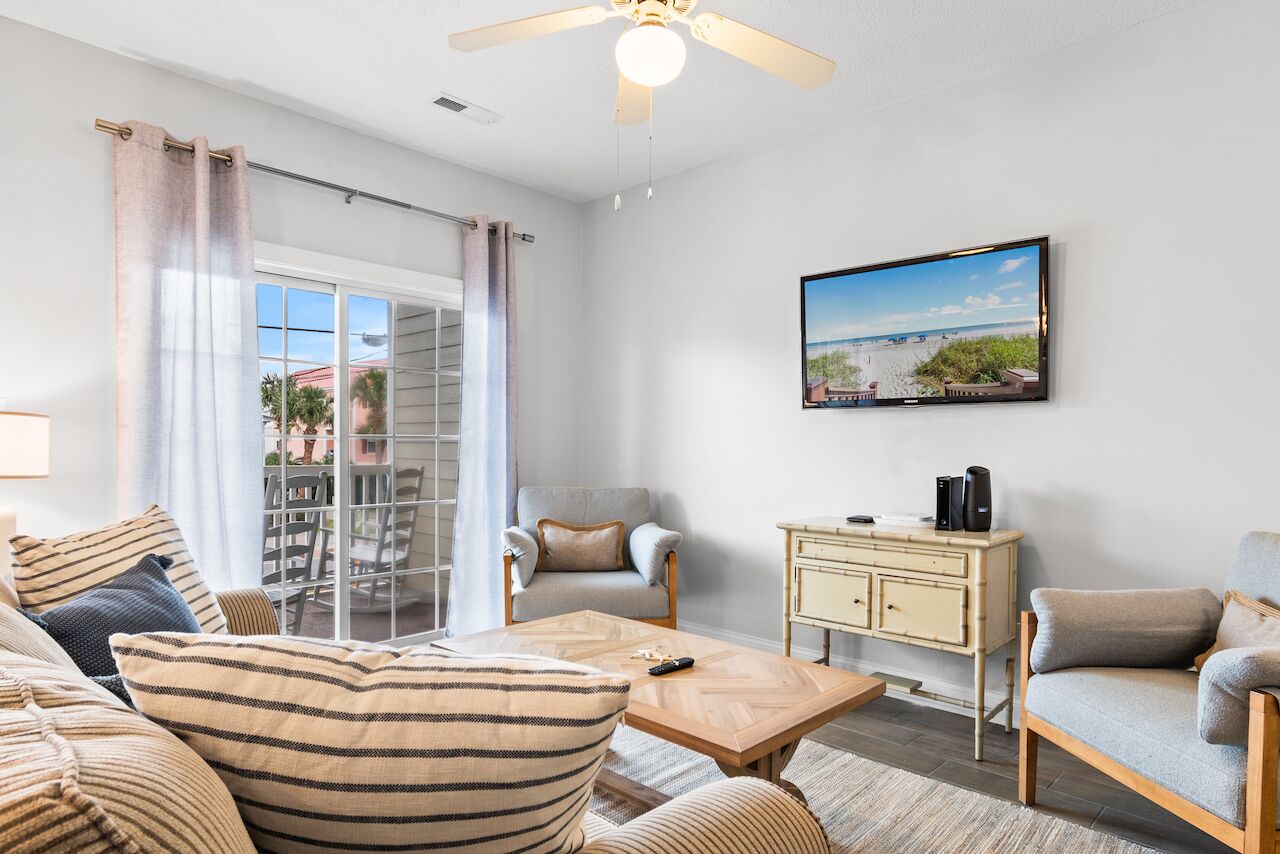 A living room with a sofa, armchair, coffee table, and a TV on the wall.