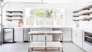 A modern kitchen with white cabinetry, a large window, and rustic wooden shelves.