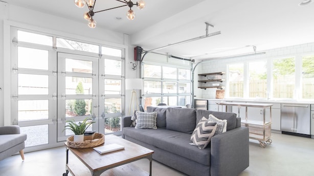 A spacious living room with a grey sofa, a coffee table, and a dining area with a kitchen in the background.