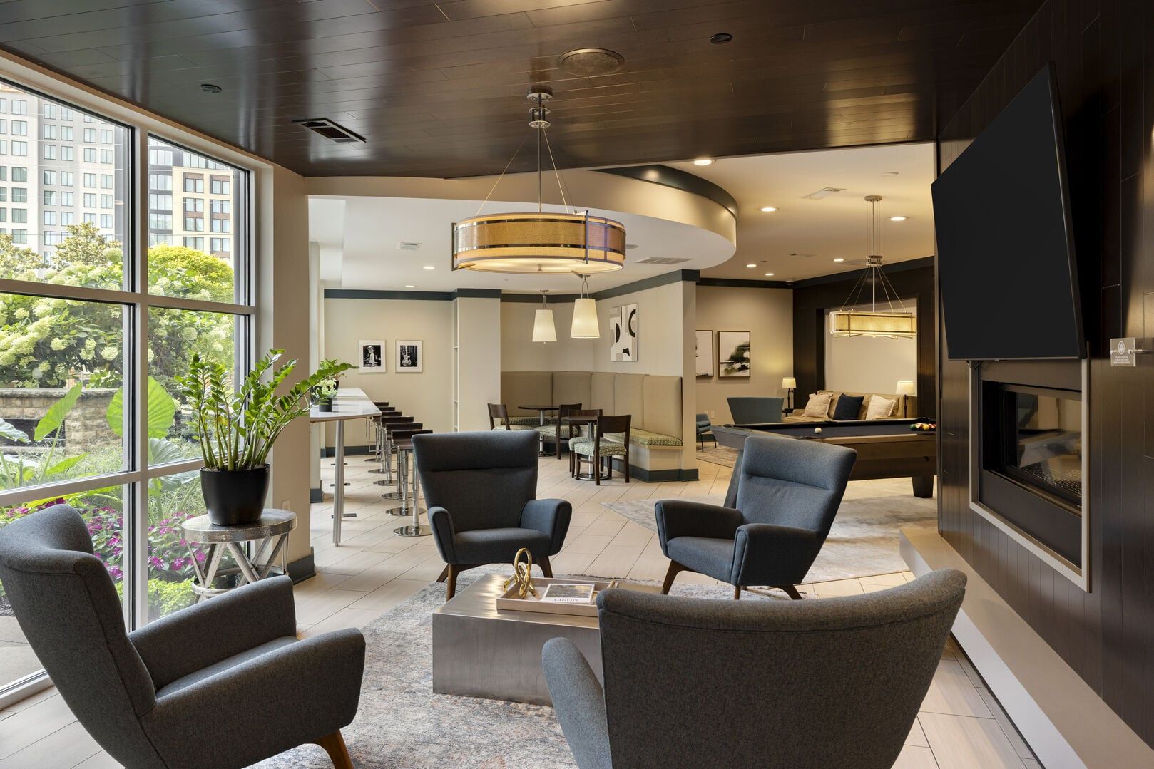 A modern hotel lobby with a seating area, a dining space, and a large TV screen.