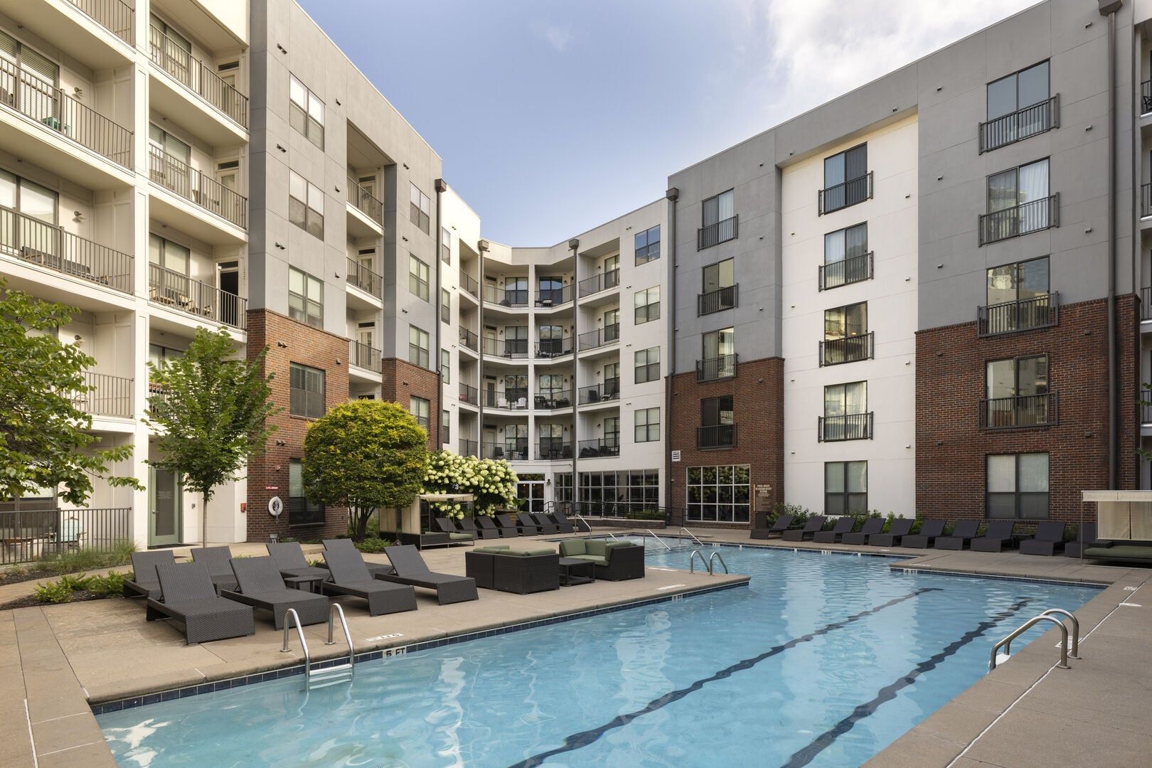 A multi-story residential building with a swimming pool, outdoor seating, and a brick facade.