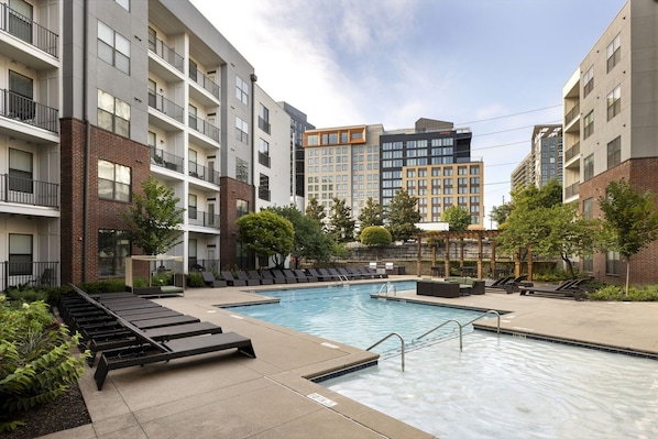 A modern apartment building with a swimming pool, outdoor seating, and a pergola.