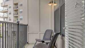 Un balcon avec deux fauteuils en osier, une rambarde en métal et une fenêtre avec des stores.