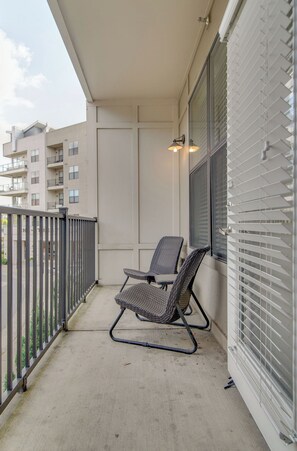 A balcony with two wicker chairs, a metal railing, and a window with blinds.